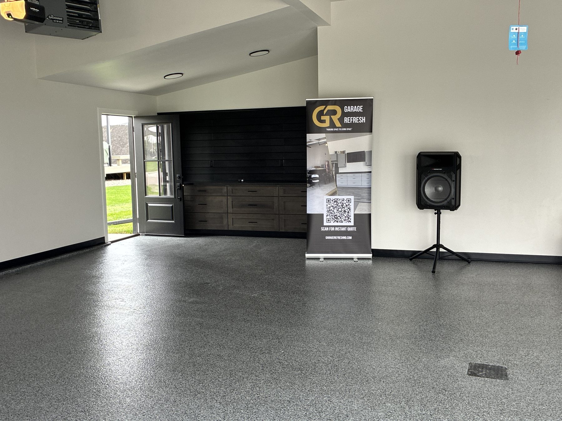 After: Mapleton, ND garage with a gray and black full-flake epoxy floor, stained gray drawer-base cabinets, dark laminate countertop and black slat wall