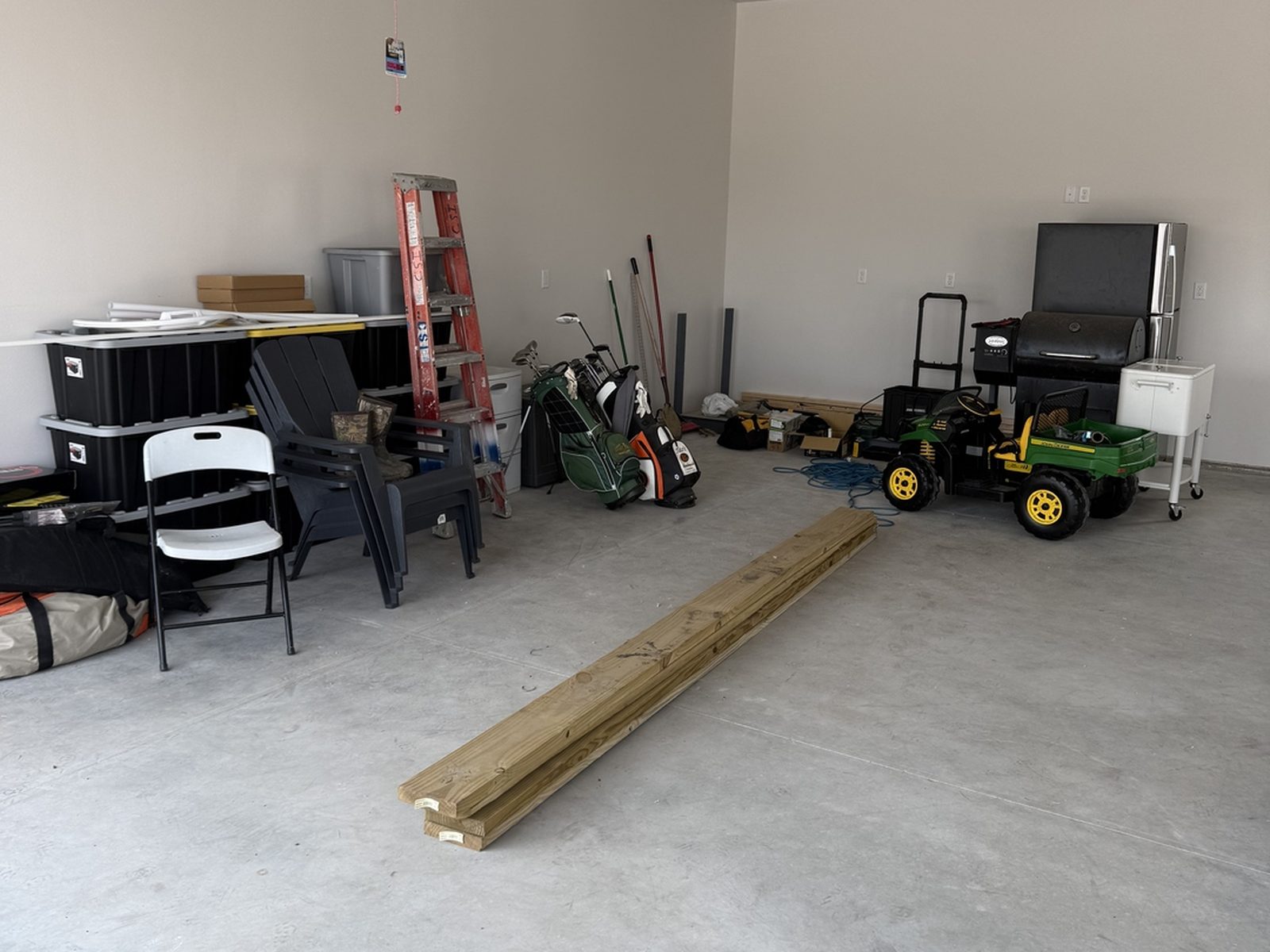Before: bare concrete garage in Mapleton, ND with storage totes, folding chairs, a ladder and golf bags piled on the floor