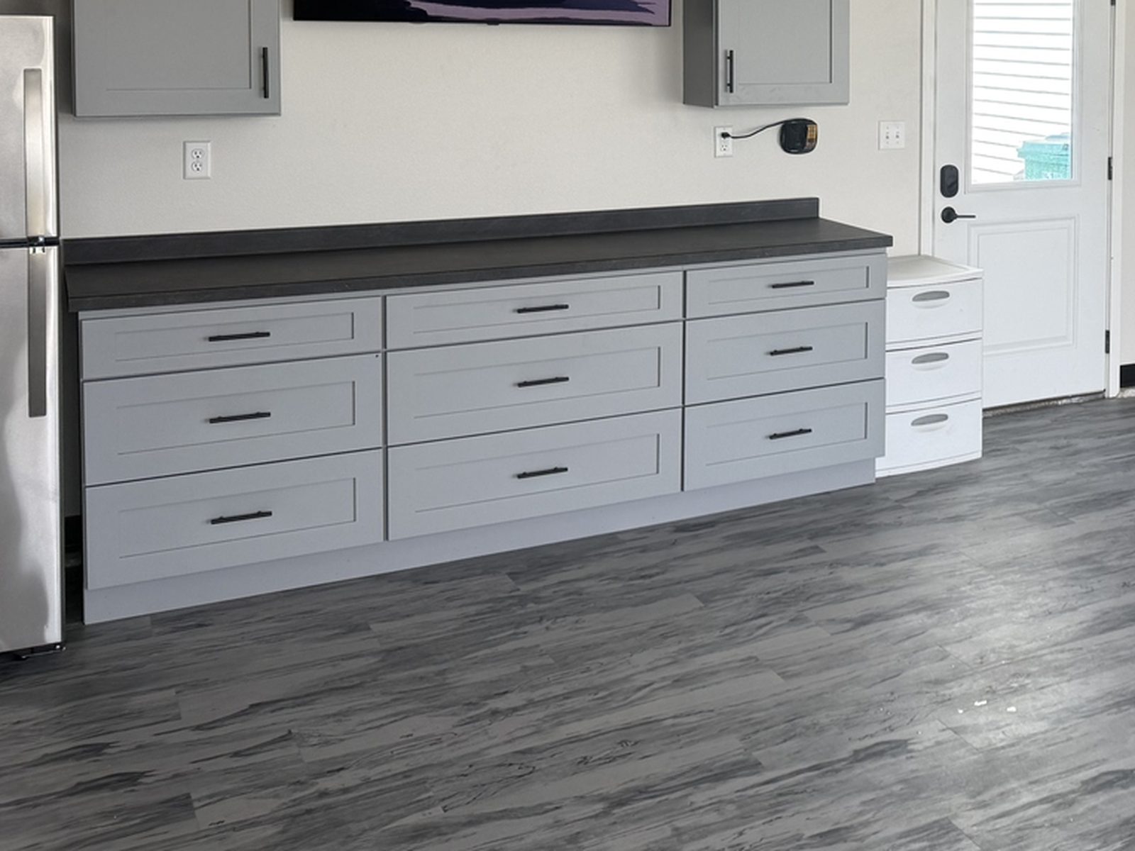 Close up of gray shaker garage base cabinets with soft-close drawers, dark laminate countertop and gray wood-look LVT flooring