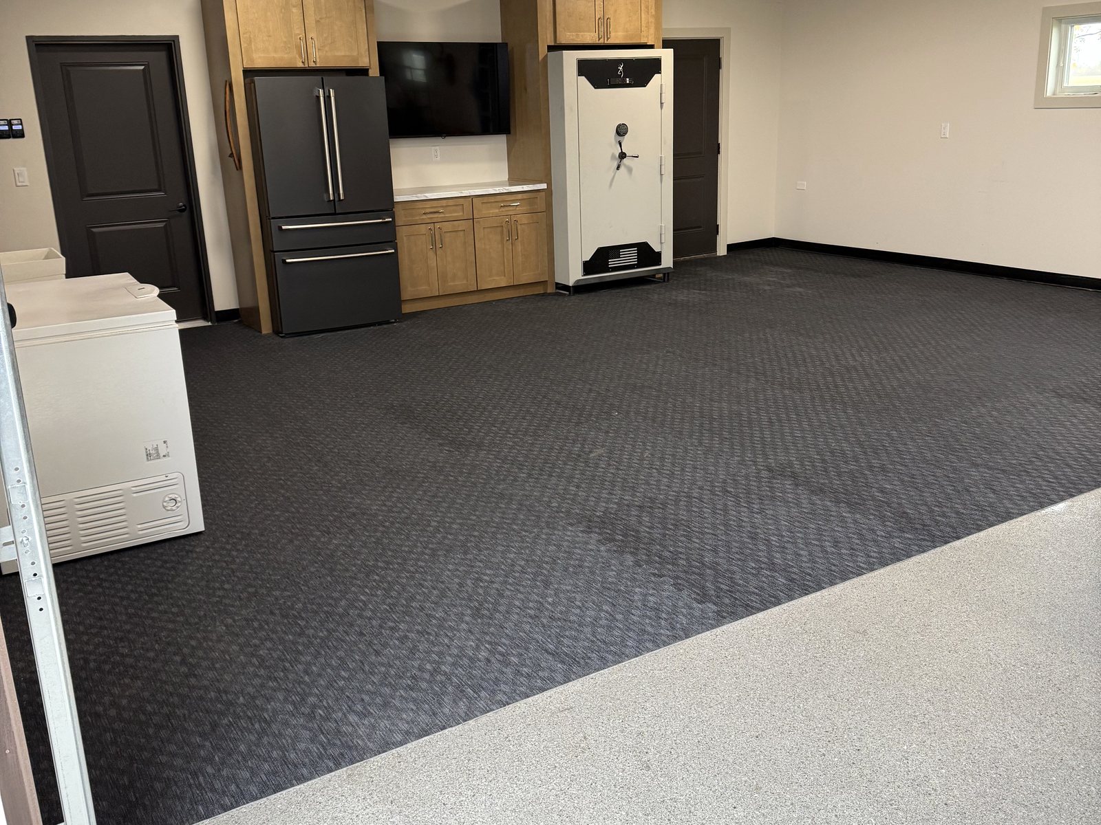After: flake epoxy floor leading into a rubber gym floor lounge zone with a finished cabinet wall in a Reiles Acres, ND garage