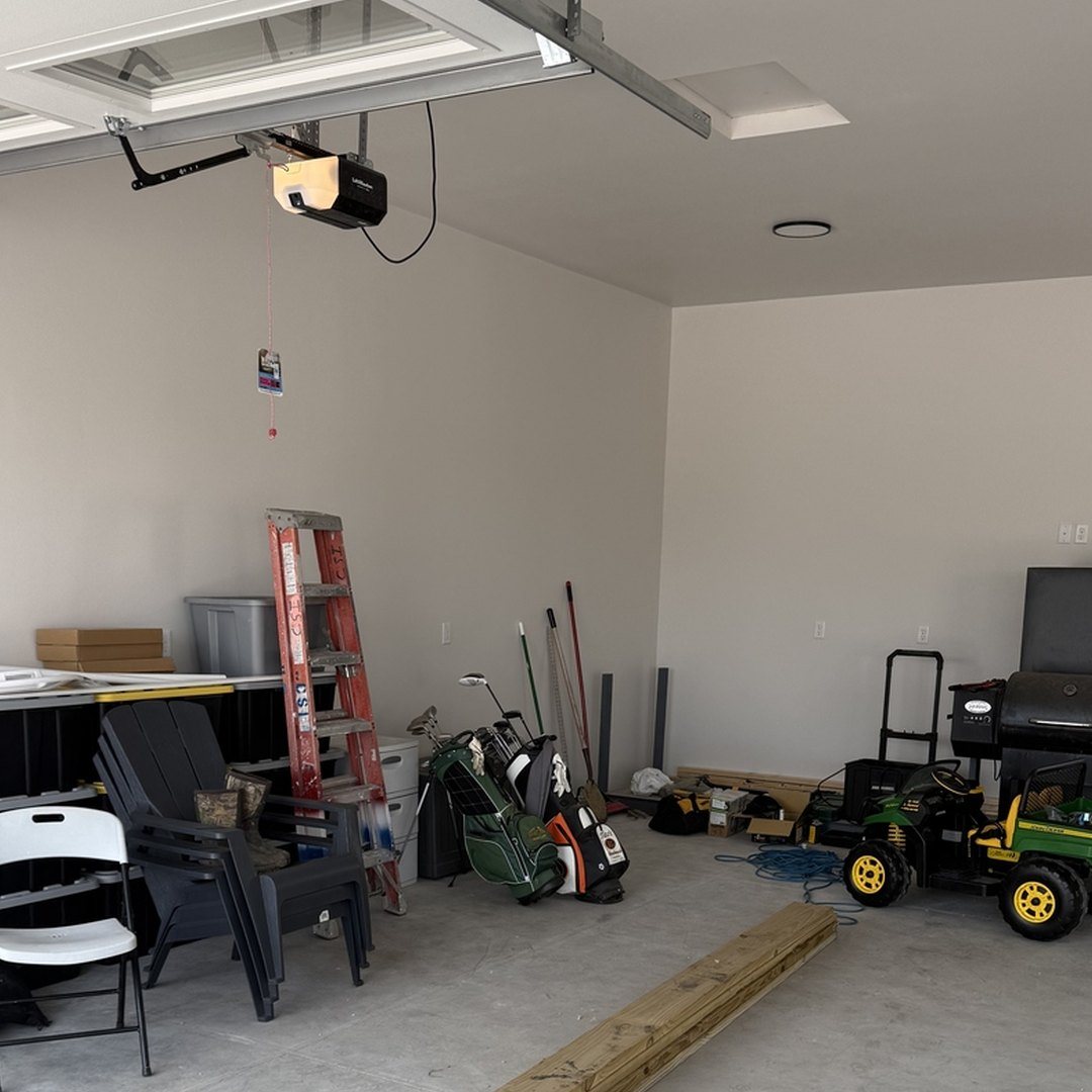 Before photo of the same Mapleton ND garage on bare concrete with storage totes, folding chairs, a ladder and golf bags piled along the wall