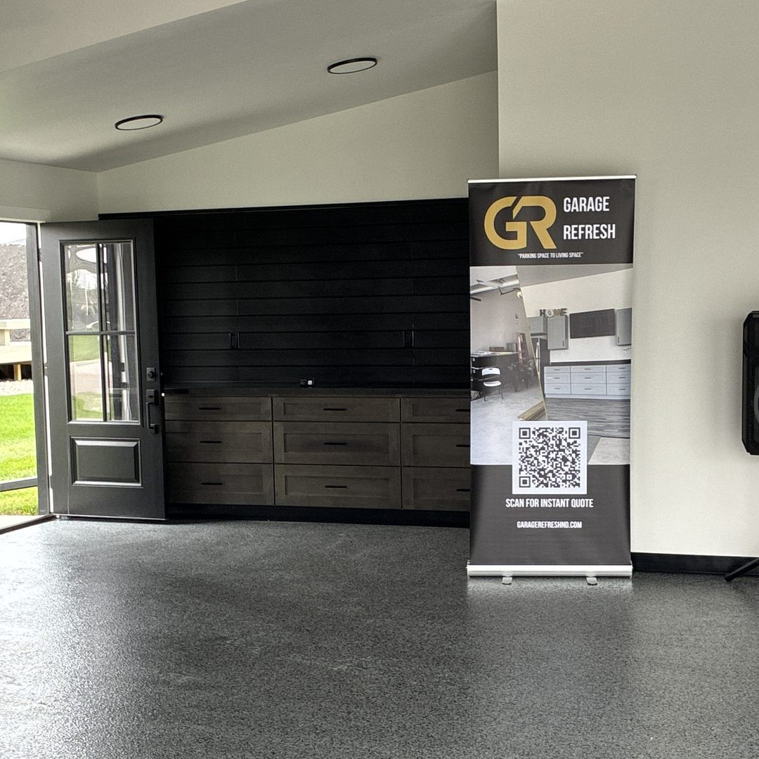 After photo of a Mapleton ND garage with a full-flake epoxy floor, stained gray drawer-base cabinets, a dark laminate countertop and a black slat wall