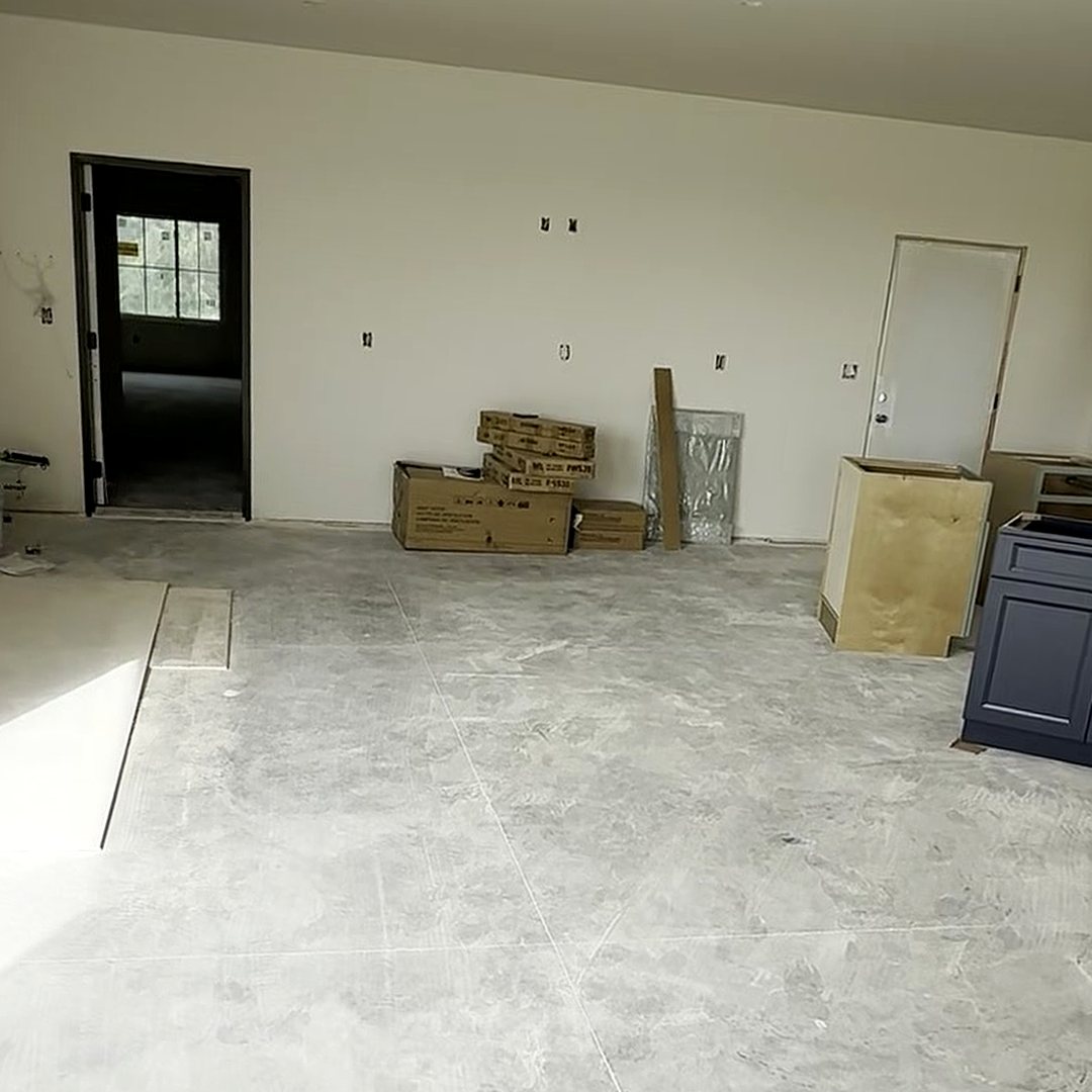 Before photo of the same lounge end with a blank drywall wall and cabinet boxes staged on bare concrete