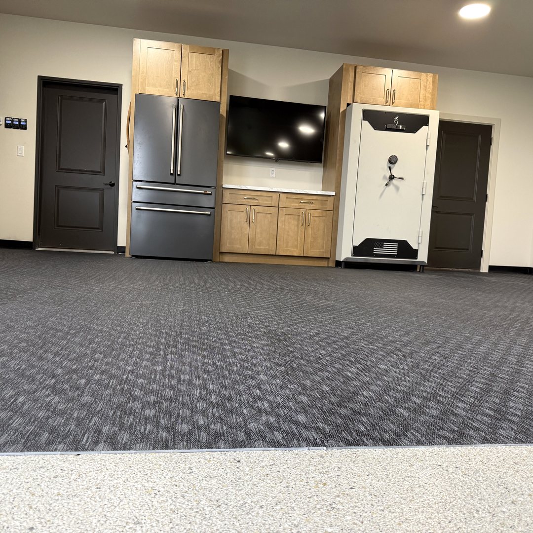 After photo of the lounge end of a Reiles Acres ND garage with a wood-tone cabinet wall around the refrigerator, TV and safe over rubber gym flooring