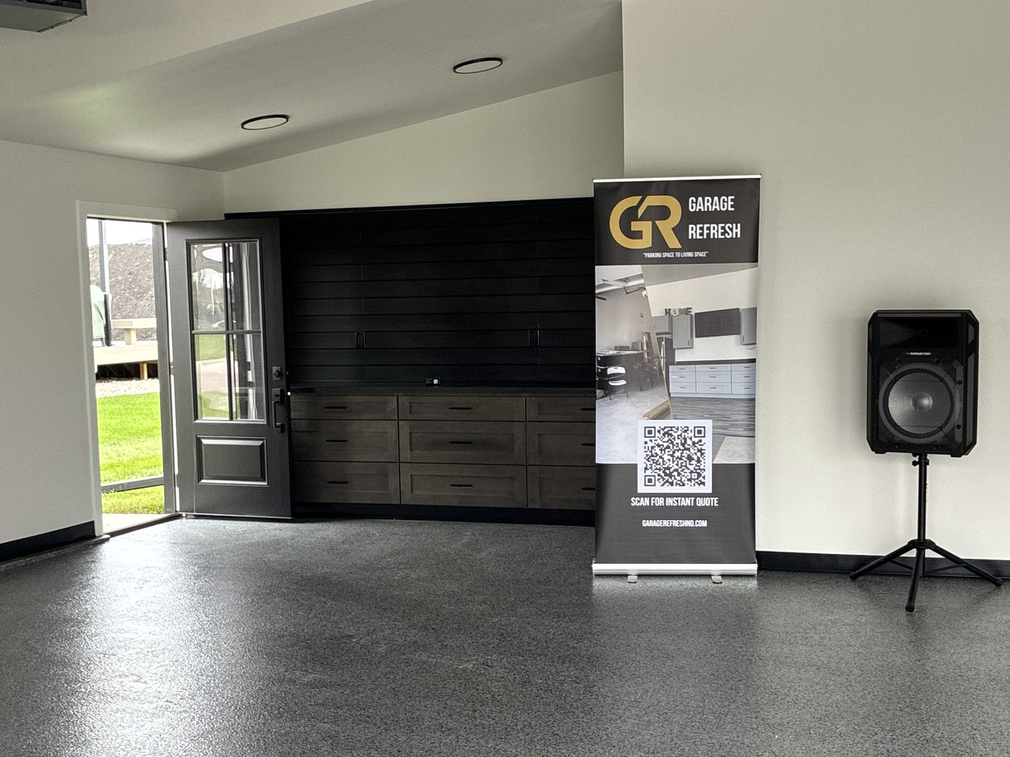 After: Mapleton, ND garage with a gray and black full-flake epoxy floor, stained gray drawer-base cabinets with a dark laminate countertop and a black slat wall on the back wall