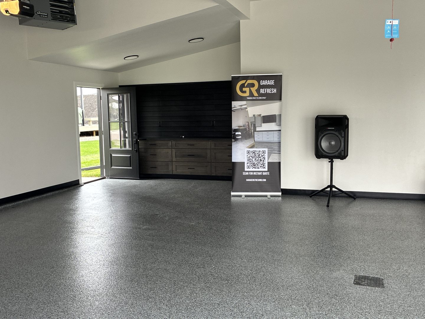 Wide after photo of a finished Mapleton ND garage with a gray and black full-flake epoxy floor, black base trim, stained gray cabinets and a black slat wall