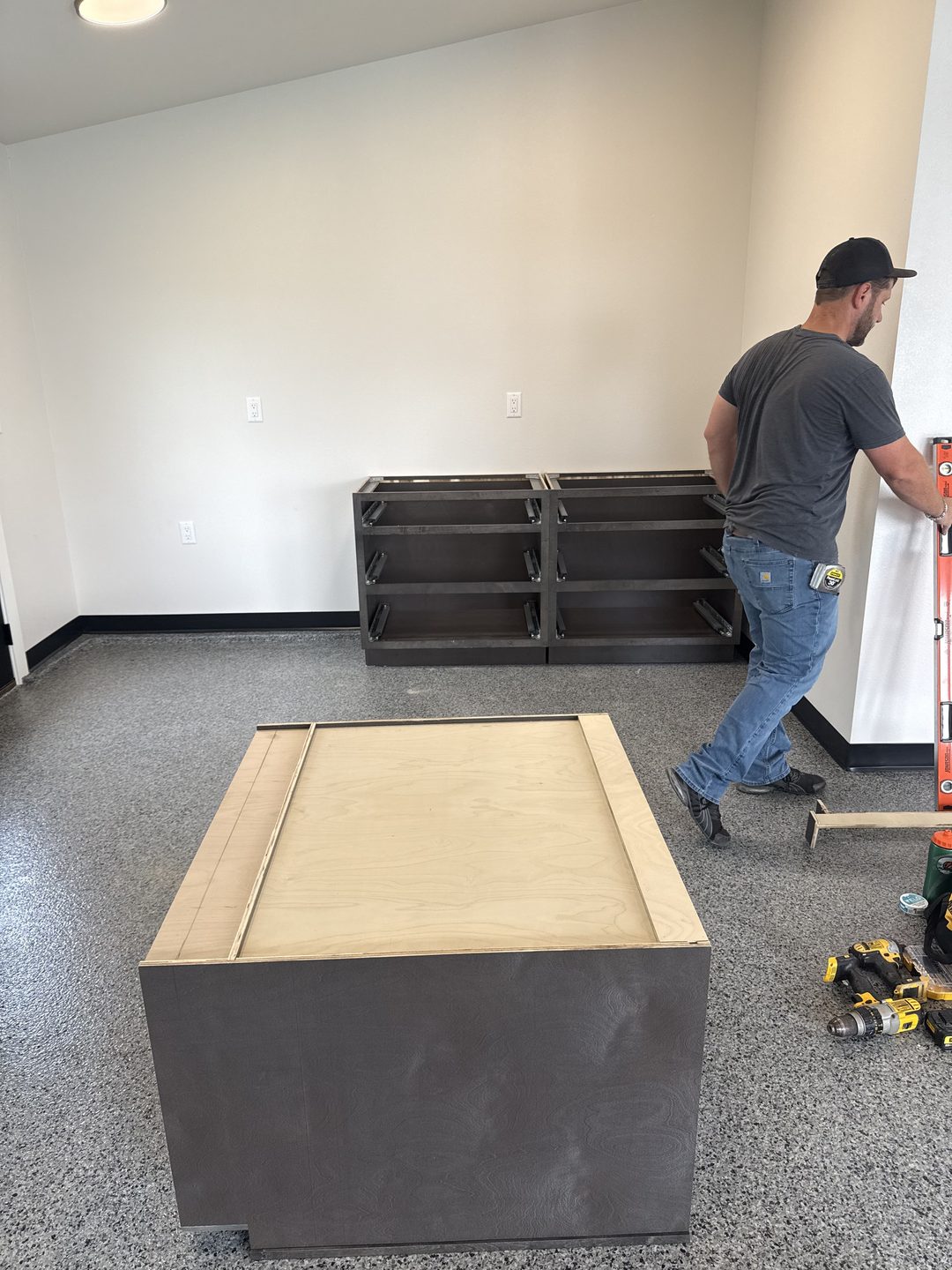 In-progress photo of a Garage Refresh installer leveling stained gray drawer-base garage cabinets on a new full-flake epoxy floor in Mapleton ND