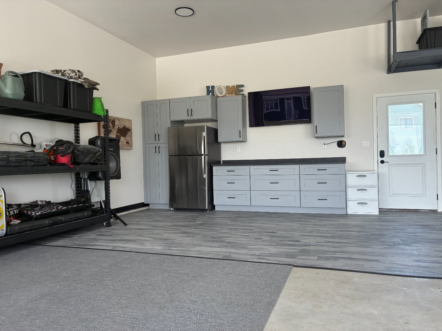 After photo of a Mapleton ND garage with black storage shelving on the left, the gray shaker garage cabinet run in the centre and the house entry door on the right above new LVT flooring