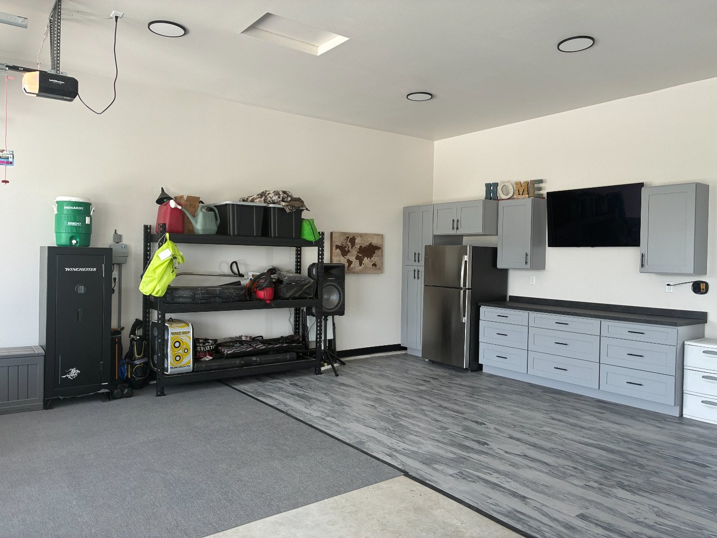 Wide after photo of a Mapleton ND garage showing the full gray shaker cabinet run with wall uppers and mounted TV above new gray wood-look LVT flooring