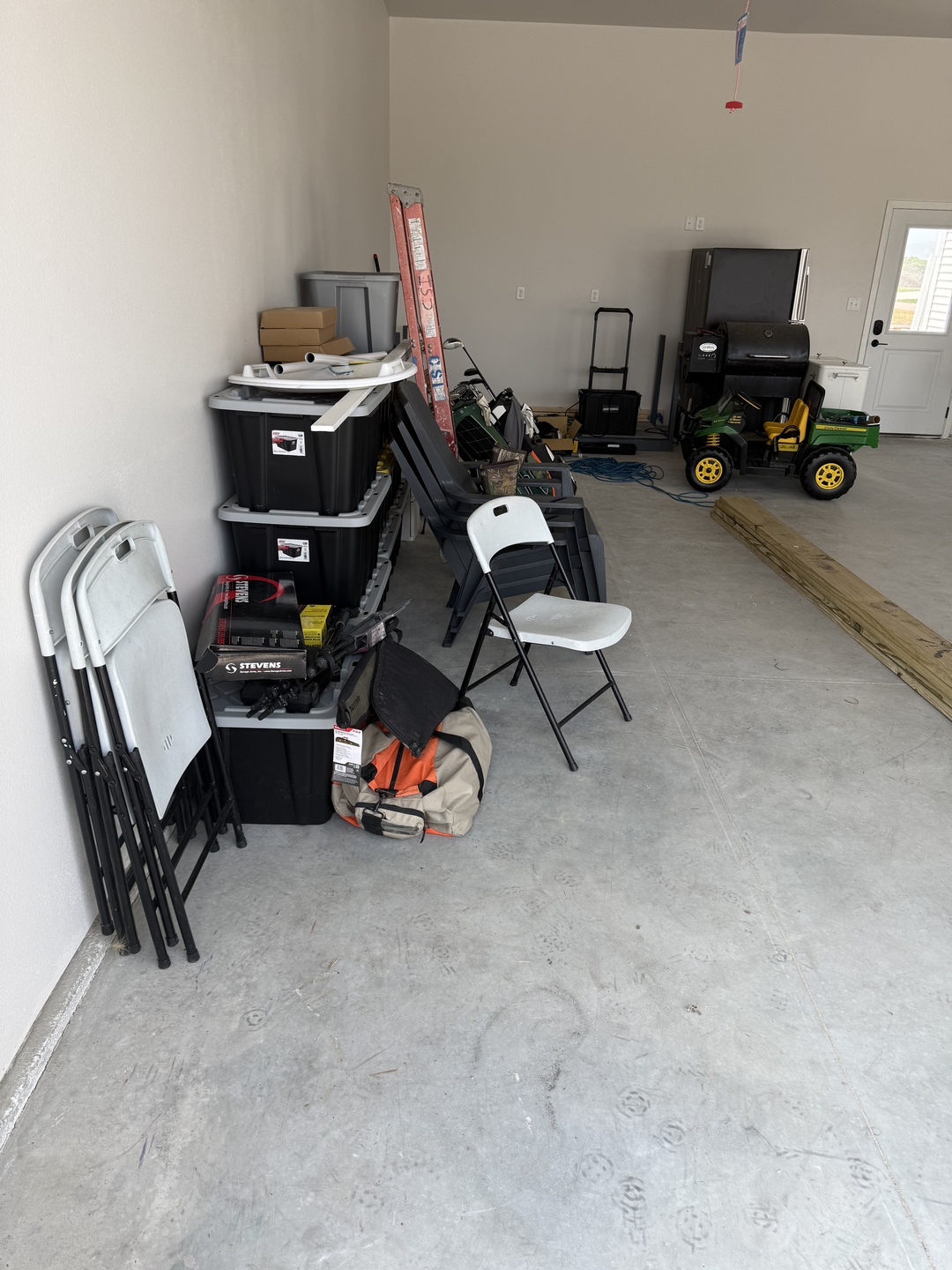 Before photo of the cluttered side wall in a Mapleton ND garage with stacked totes and folding chairs on bare concrete where garage cabinets were installed