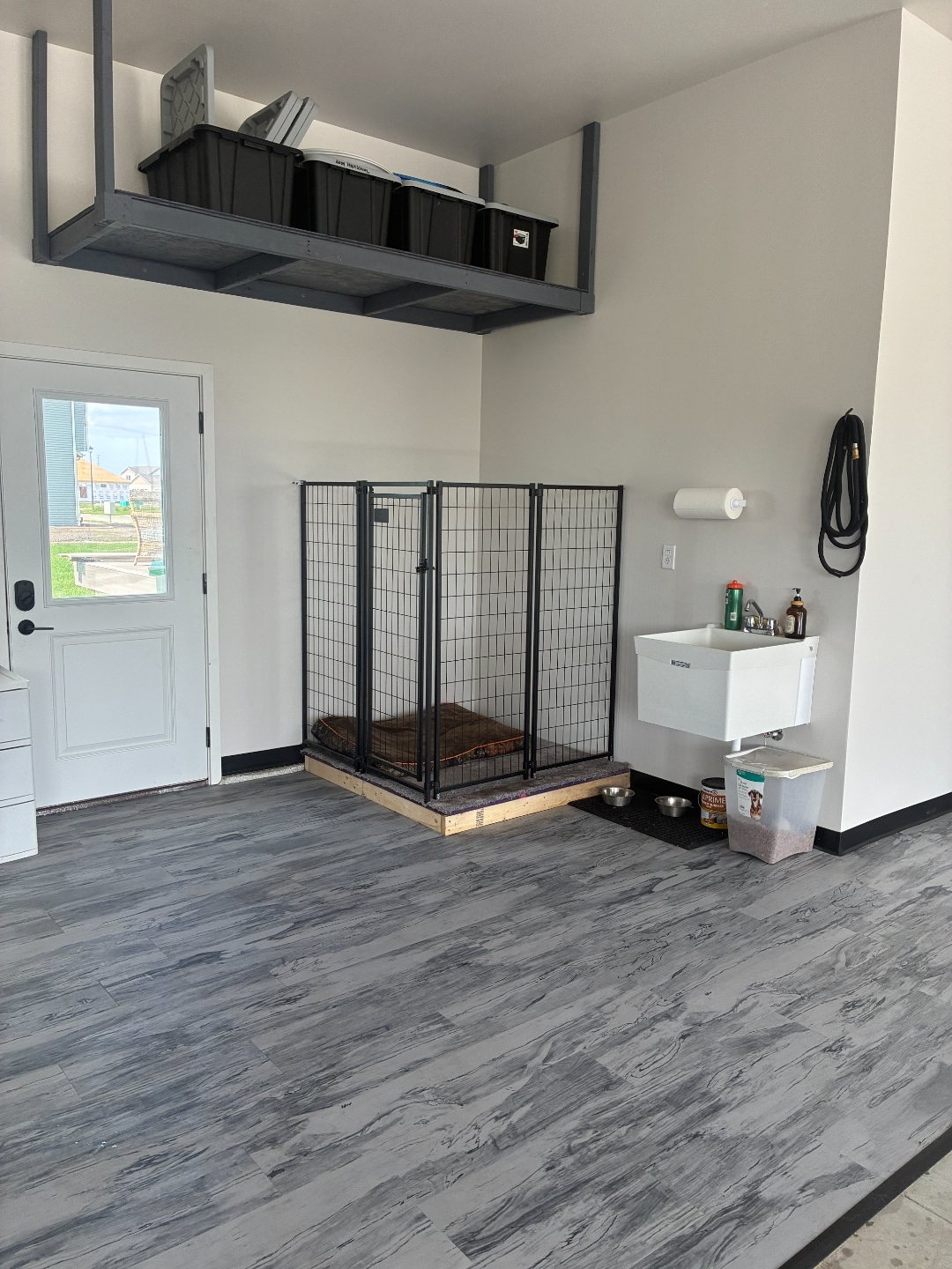 After photo of the storage add-ons in a Mapleton ND garage: a gray overhead storage rack, a wall-mounted utility wash sink and a dog kennel corner beside the house entry door