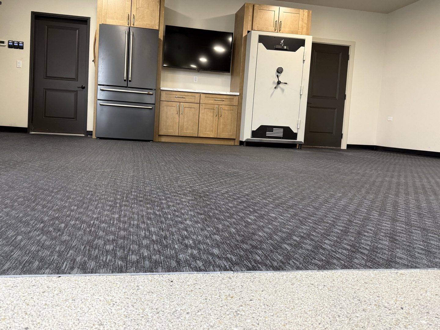 After: the same lounge end finished with a wood-tone cabinet wall around the refrigerator, TV and safe, rubber gym flooring, black vinyl base and the flake epoxy edge in front