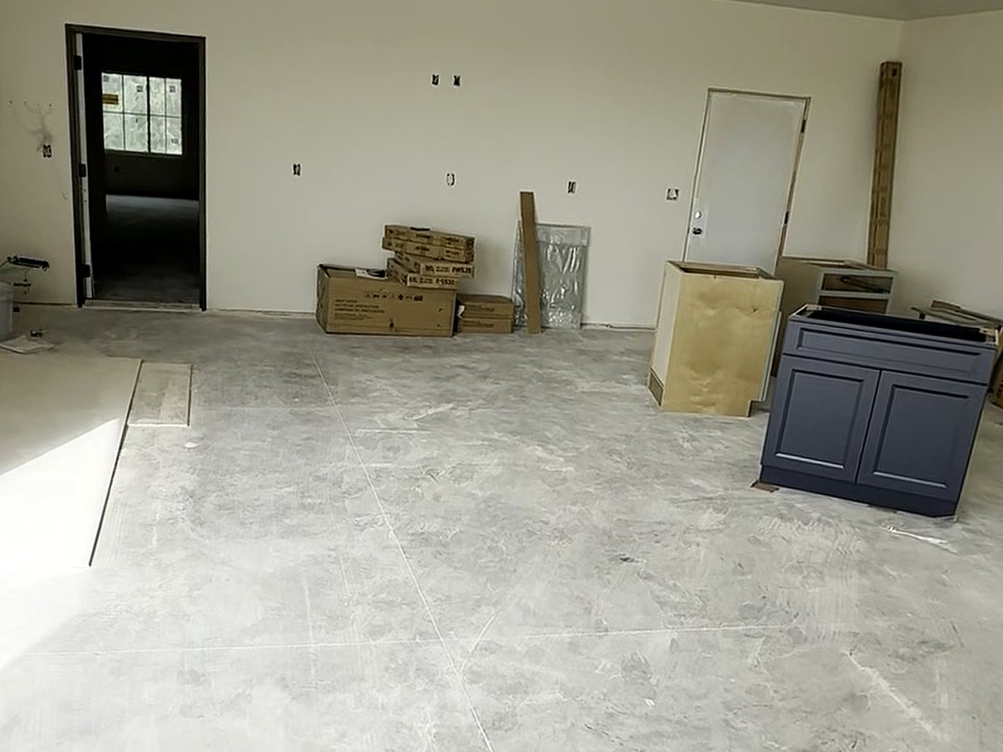 Before: the lounge end of the Reiles Acres, ND garage in August, a blank drywall wall between two doorways with electrical roughed in, cabinet boxes staged on bare concrete