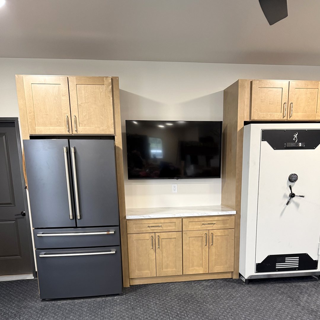 Finished: the cabinet wall with uppers, a white laminate countertop, the TV mounted between the refrigerator and safe, over rubber gym flooring