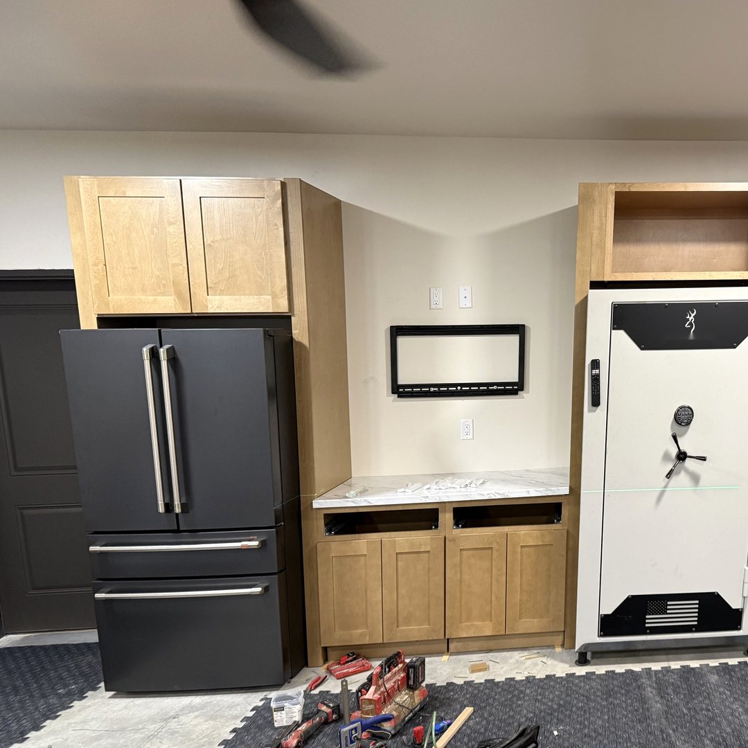 Install day: wood-tone cabinets set around the refrigerator and safe, with the TV mount on the wall and tools on the floor