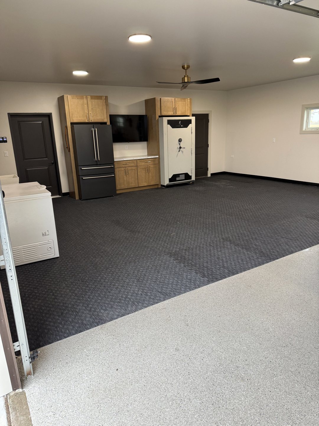 After photo looking across the flake epoxy floor into a rubber gym floor lounge zone with a finished cabinet wall, TV and black vinyl base in a Reiles Acres ND garage