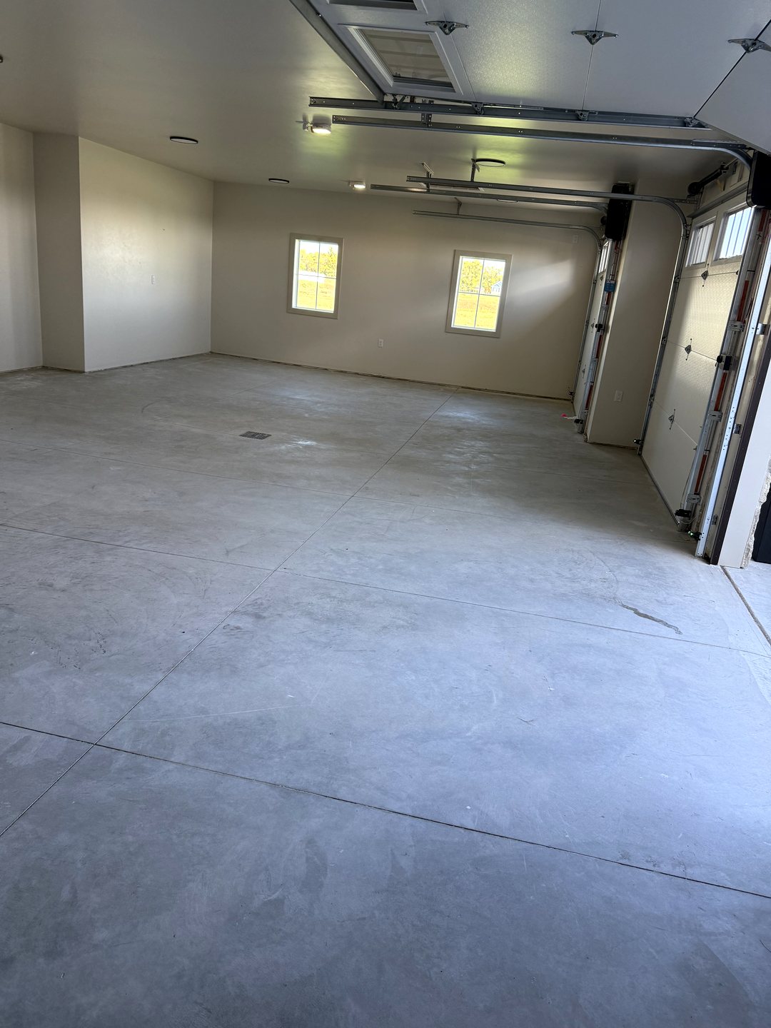 Before photo of a large Reiles Acres ND garage from the overhead door with bare gray concrete, control joints and blank white walls