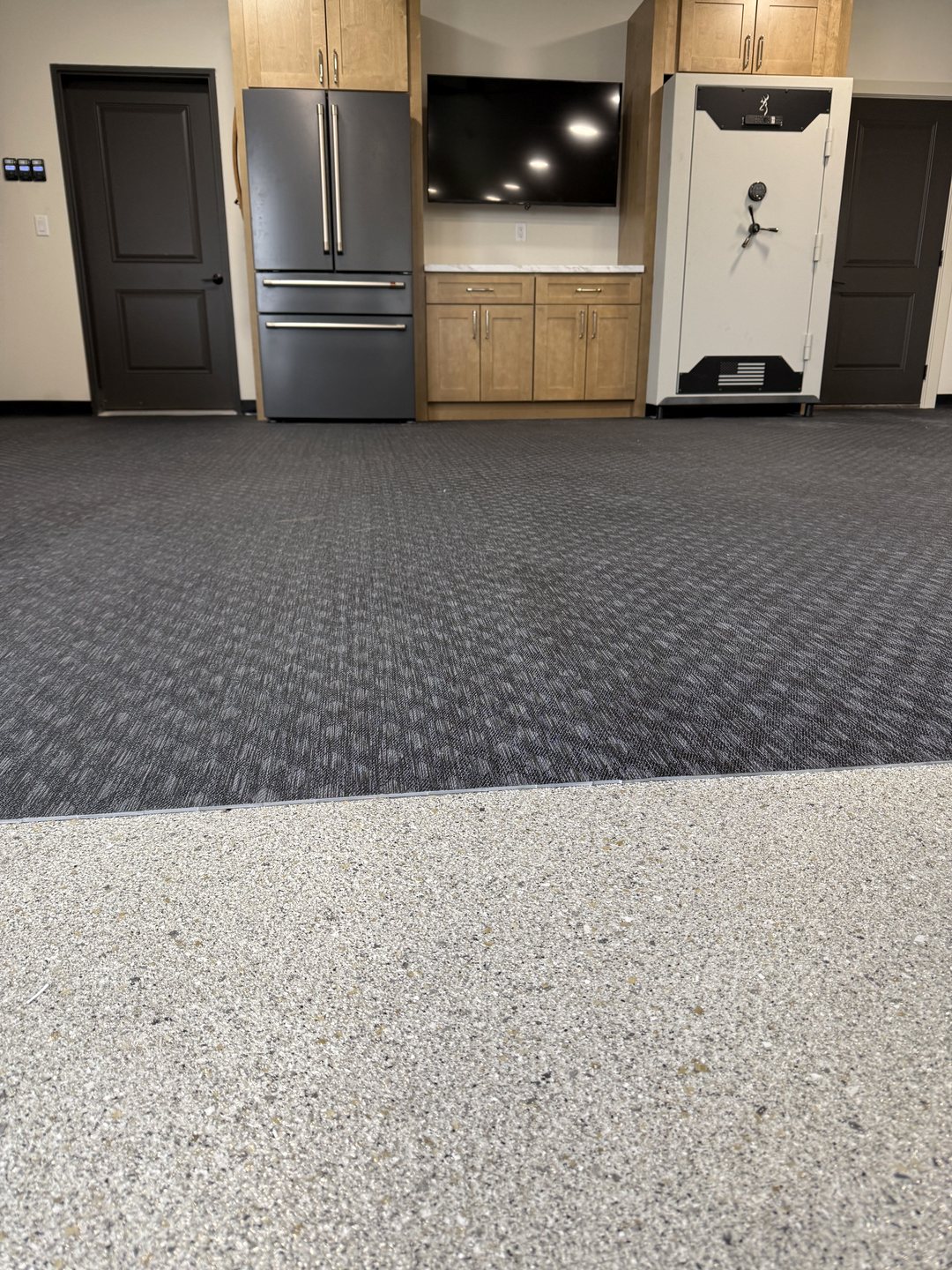 Photo of the clean edge where a flake epoxy floor meets interlocking rubber gym flooring in front of the cabinet wall in Reiles Acres ND