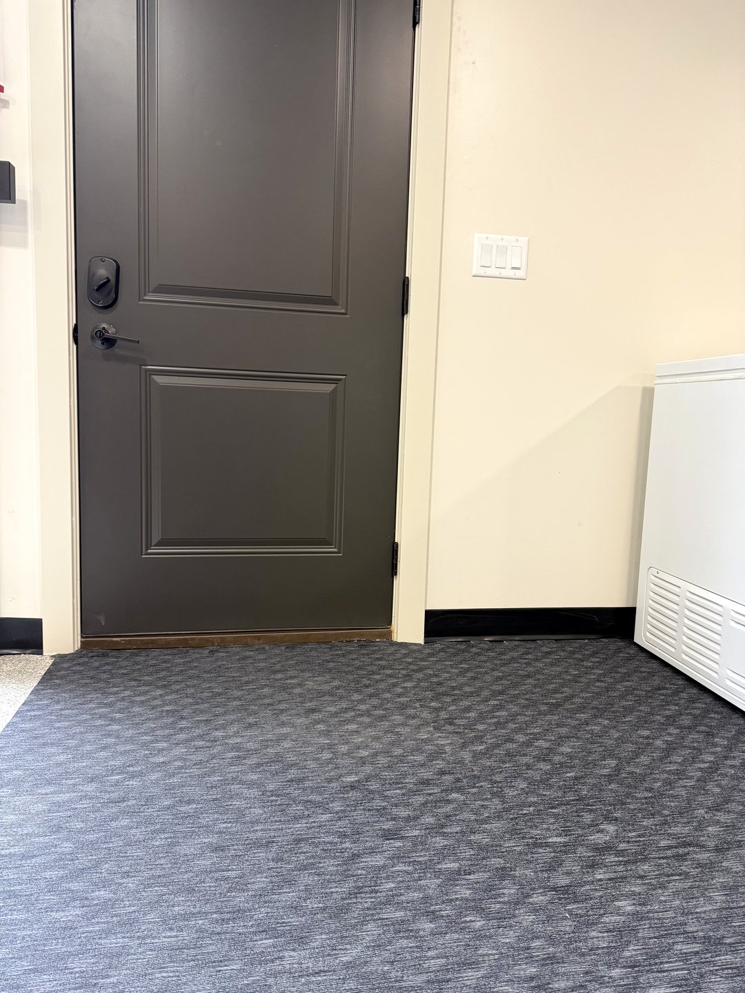 Close photo of black vinyl base trim along the wall at a dark entry door over rubber gym flooring in Reiles Acres ND