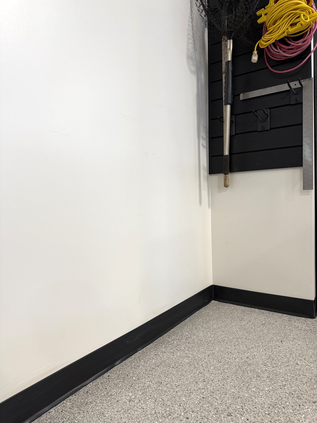 Close photo of black vinyl base where a white wall meets the flake epoxy floor next to a slat wall in Reiles Acres ND
